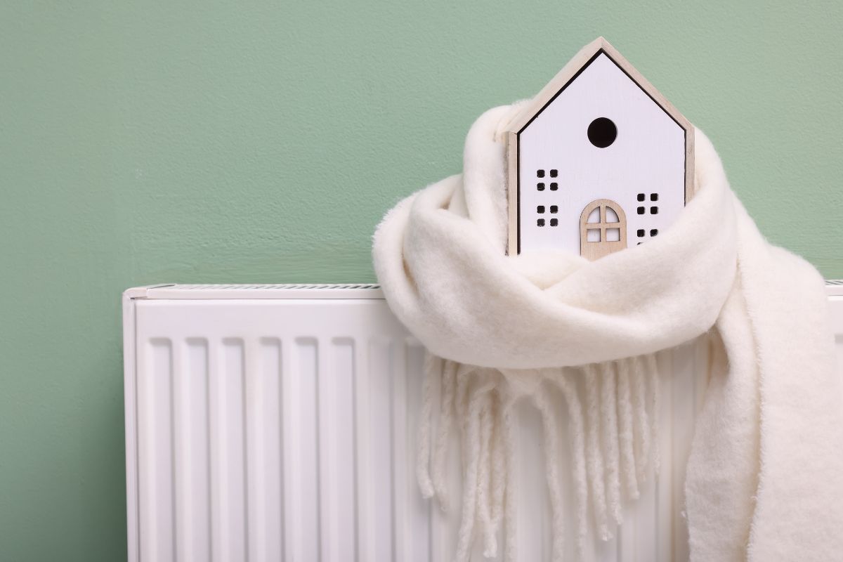Isolatie en warmtebehoud gesymboliseerd door een houten huisje met een sjaal naast een radiator.